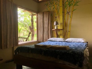 Relax in a serene space with a comfortable bed, a table, and a window offering a view of lush greenery.