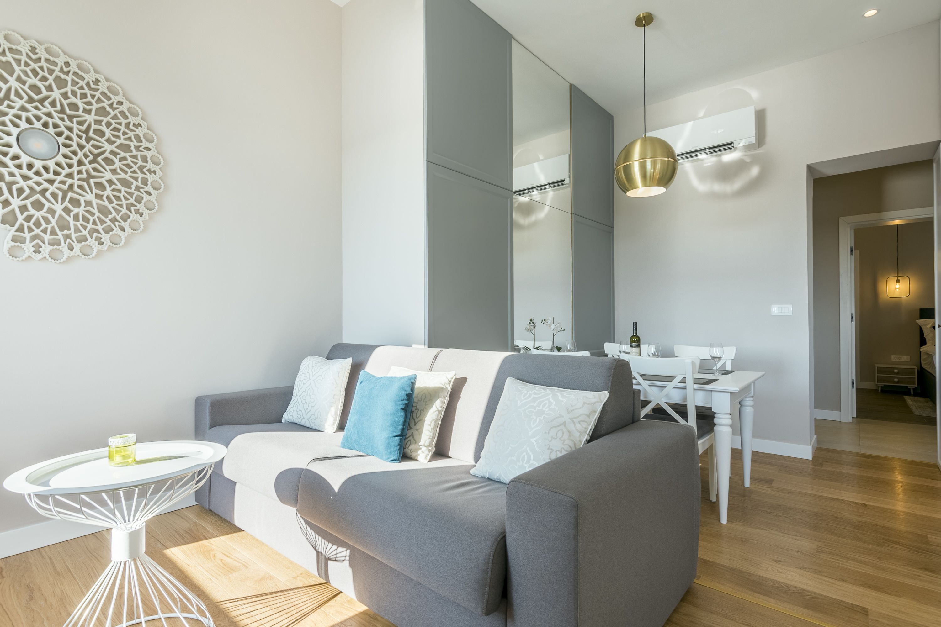 Ein modernes Wohnzimmer mit grauem Sofa, einem weißen Couchtisch und einem Essbereich mit weißem Tisch und Stühlen.