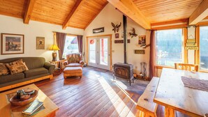 A cozy cabin interior with a wooden ceiling, a sofa, a table, and a fireplace.