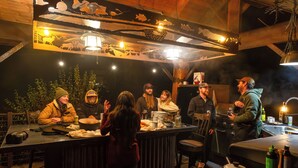 A rustic bar area with wooden beams, a large pot on the counter, and a group of people gathered around.