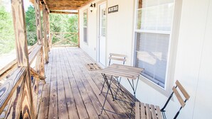 Una terraza de madera con una mesa y sillas, un letrero que dice “The Cabin Shack”, y vistas a árboles a través de las ventanas.