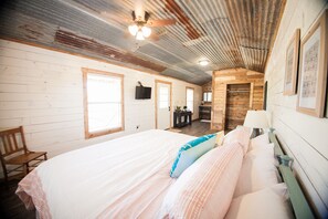 Une chambre avec un grand lit, des murs en bois, un ventilateur de plafond et un petit coin bureau.