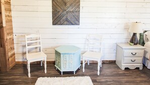 Una habitación con dos sillas blancas, un mueble azul, una mesita de noche blanca y un tapete blanco.