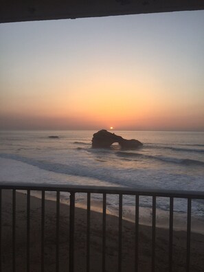 A sunset view from a balcony with a railing, overlooking the ocean and a rocky formation. - Fantastic ocean view, in the heart of Biarritz. (Biarritz)