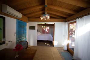 Ein Zimmer mit Holzboden, einem Bett mit weißer Bettwäsche, einem Sessel, einem kleinen Tisch und einer Vase mit Blumen.