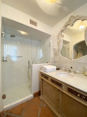 Un baño con ducha envuelta en vidrio, un espejo grande y un lavabo de mármol.