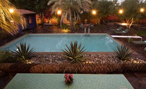 Un área de piscina con borde de piedra, sillas de descanso y una mesa con sillas.