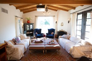 Ein gemütliches Wohnzimmer mit hohen Decken, zwei blaue Sessel, ein weißes Sofa, ein Couchtisch mit Dekoration und ein Kamin.