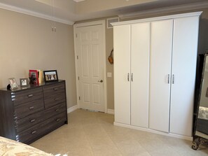 A bedroom with a dark wooden dresser, a white wardrobe, and a bed with a patterned bedspread.