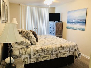Cozy retreat with a neatly made bed, television, and seascape painting.