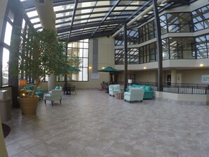 Relax in a spacious indoor area with a high ceiling and glass roof, surrounded by seating arrangements and a central potted plant.
