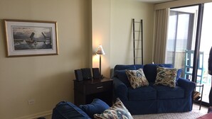 A living room with a blue sofa set, a small table, a lamp, a ladder, and a framed picture on the wall.