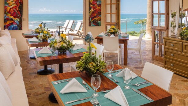 A dining area with a view of the ocean, featuring tables set with white napkins, silverware, and glassware. - Dramatic sea view and exclusive island beach - room with sea view # 2 (Ojochal)