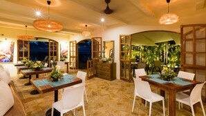 A dining area with wooden tables and white chairs, stone flooring, and pendant lighting. - Dramatic sea view and exclusive island beach - room with sea view # 2 (Ojochal)