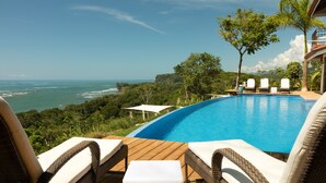 A pool with a view of the ocean, surrounded by wicker lounge chairs and a wooden deck. - Dramatic sea view and exclusive island beach - room with sea view # 2 (Ojochal)