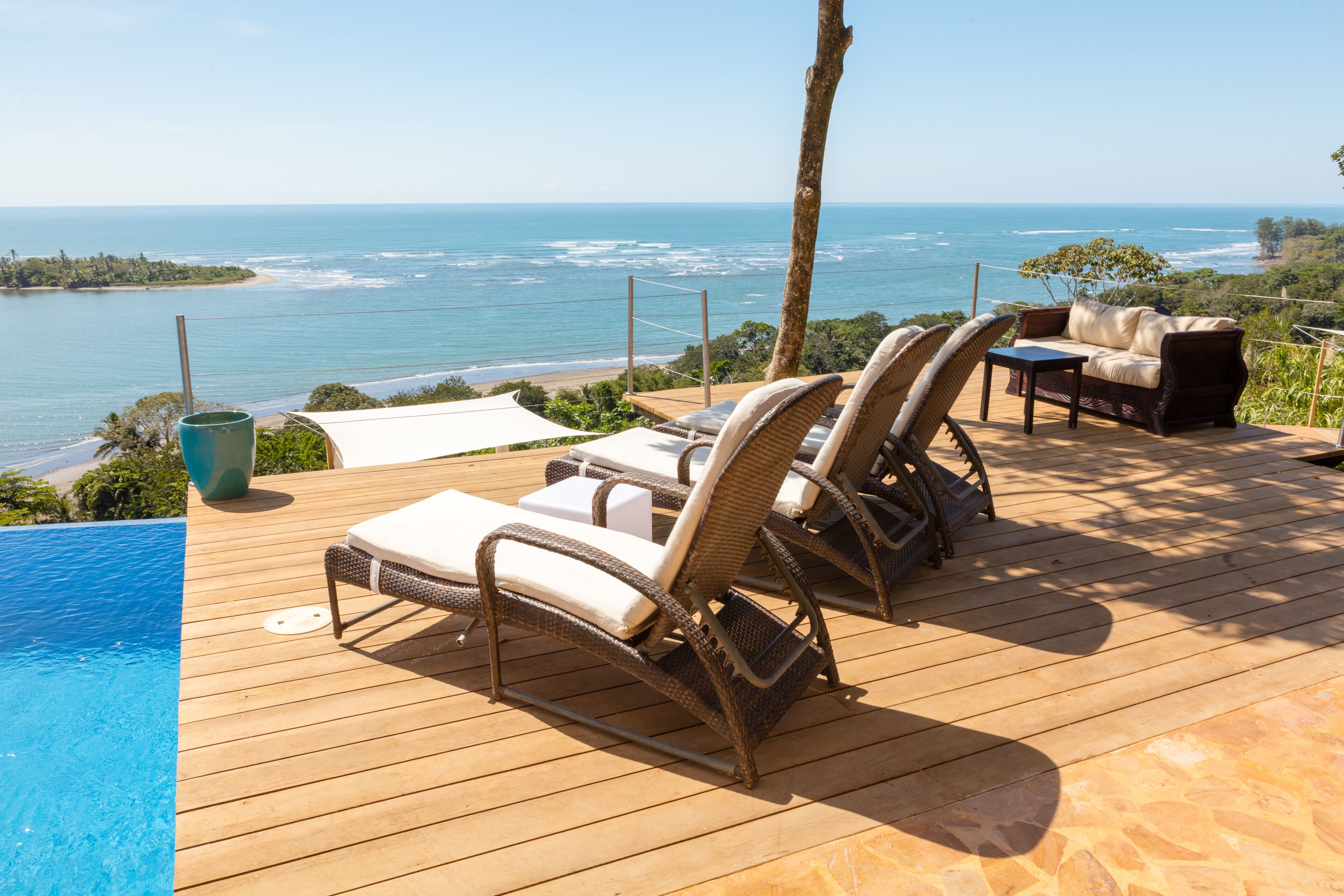 Een houten terras met lounge fauteuils en een kleine tafel, met uitzicht op een strand en de oceaan.