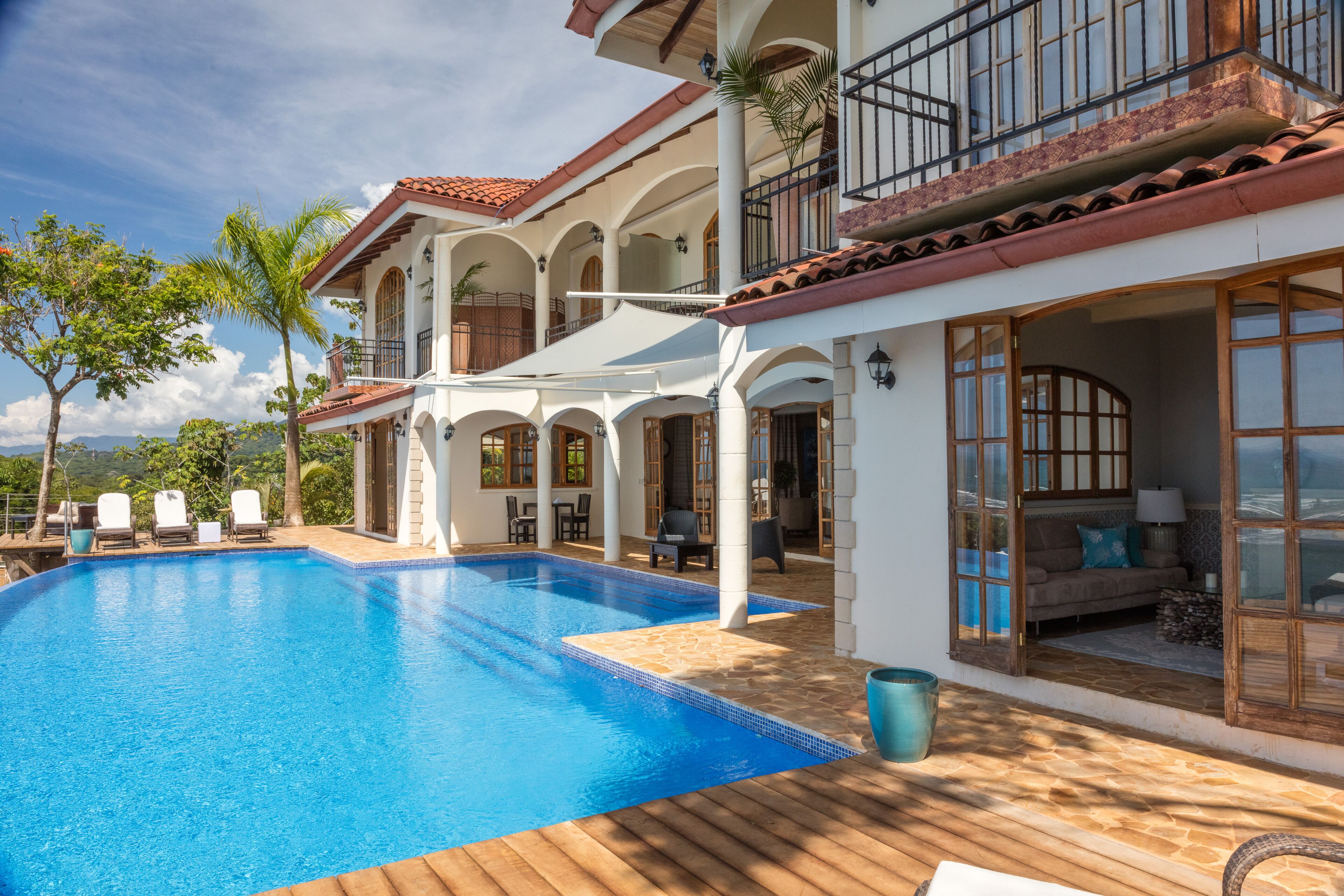 Un área junto a la piscina con una piscina azul cristalina, columnas blancas y una cubierta de madera.