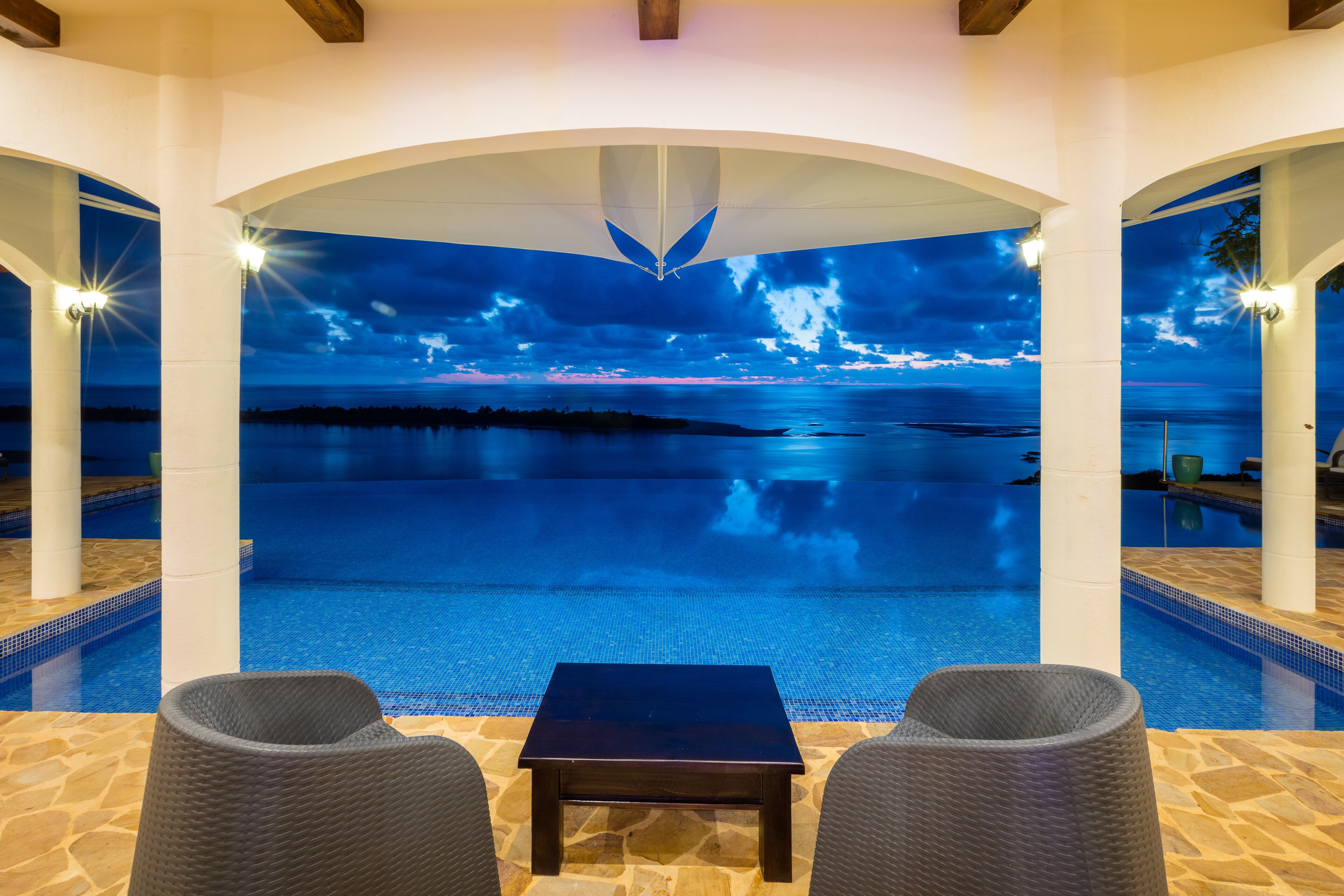 Un espace piscine avec vue sur la mer, une table et deux chaises.