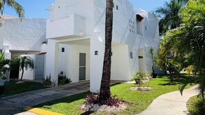 A white building with a flat roof, a central entrance, and a small garden area with palm trees. - Feb 25th onward avail 150Mbps Wifi 7 Bikes Beach Access Rare Find Contact me 🏖 (Playa del Carmen)
