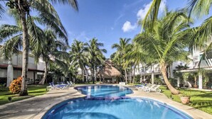 A swimming pool surrounded by palm trees and lounge chairs, with a thatched-roof structure in the background. - Feb 25th onward avail 150Mbps Wifi 7 Bikes Beach Access Rare Find Contact me 🏖 (Playa del Carmen)