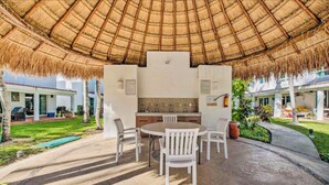 An outdoor patio with a thatched roof, a round table, and white chairs. - Feb 25th onward avail 150Mbps Wifi 7 Bikes Beach Access Rare Find Contact me 🏖 (Playa del Carmen)