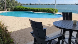 A poolside area with a view of the ocean, a covered seating area with chairs, and a table.