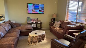 A living room with brown leather sofas, a coffee table, a TV mounted on the wall, and a window with blinds. - BEAUTIFUL MTN VIEW , HOT TUB & NEAR GOLF (Laveen)