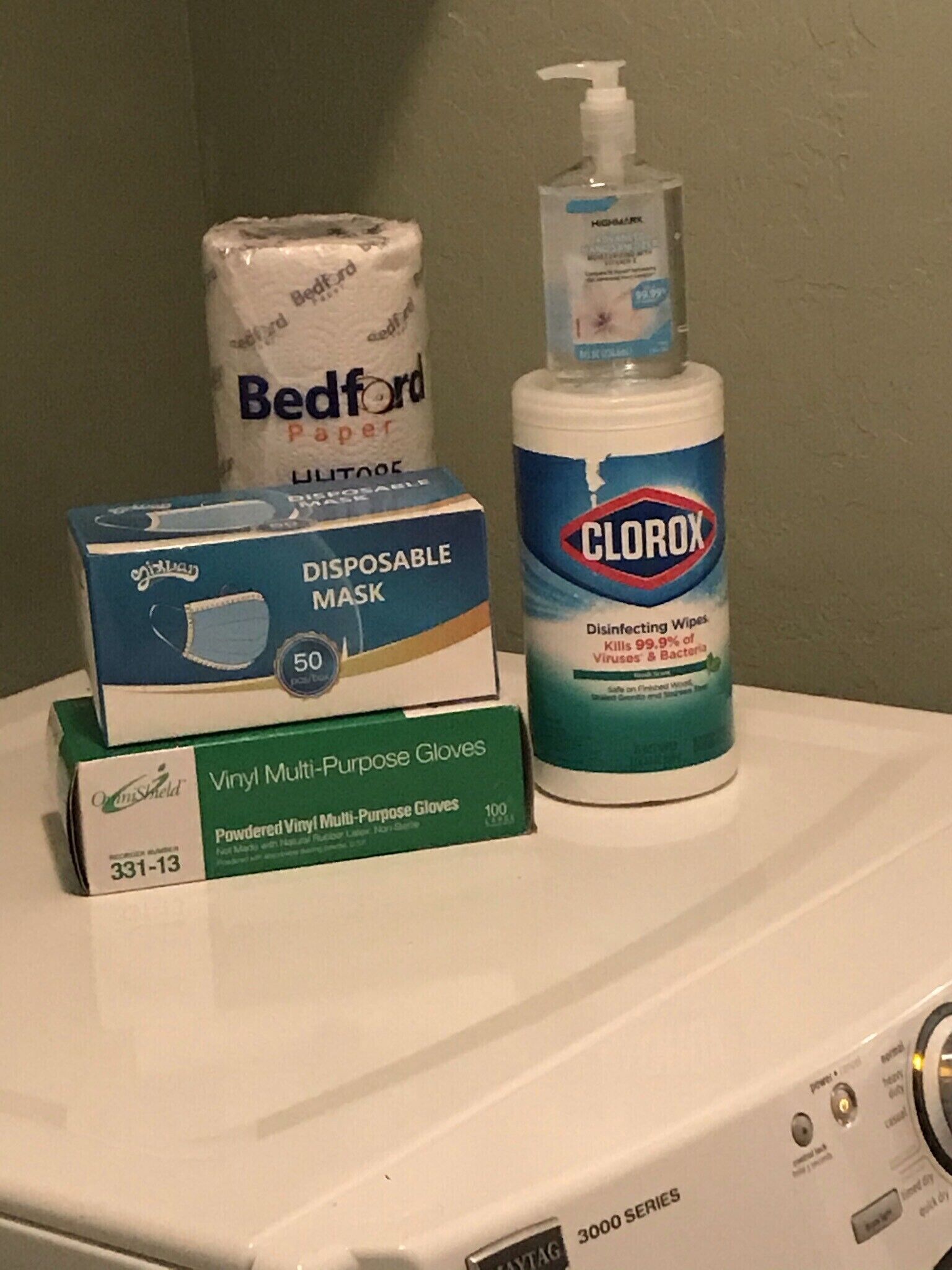 A stack of disposable items including a mask, gloves, and a bottle of Clorox wipes on a washing machine.
