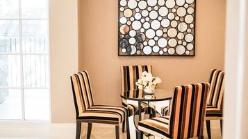 A dining area with striped chairs and a glass table, featuring a circular mirror artwork on the wall.