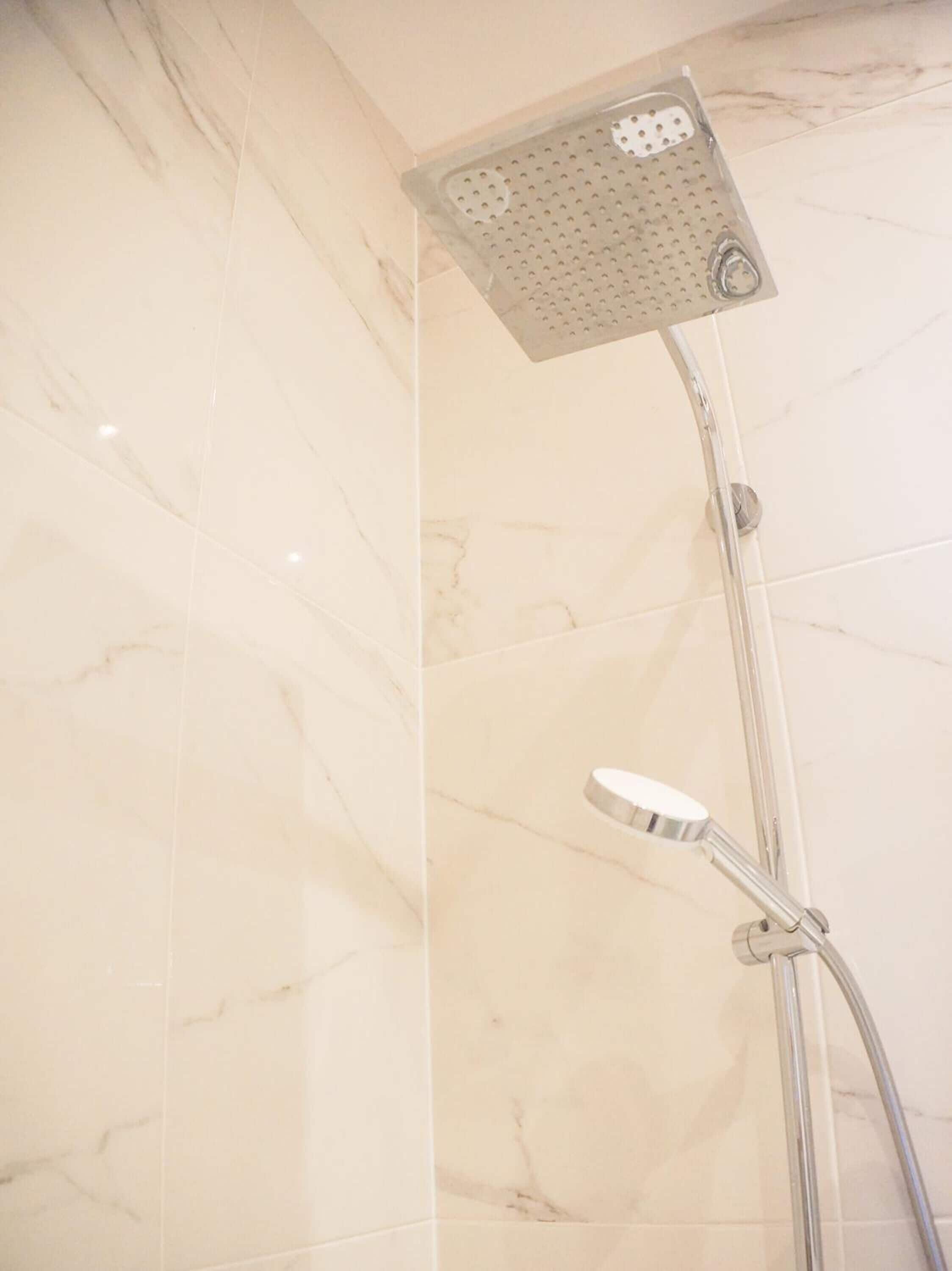 A showerhead with a square, perforated design mounted on a wall with marble tiles.