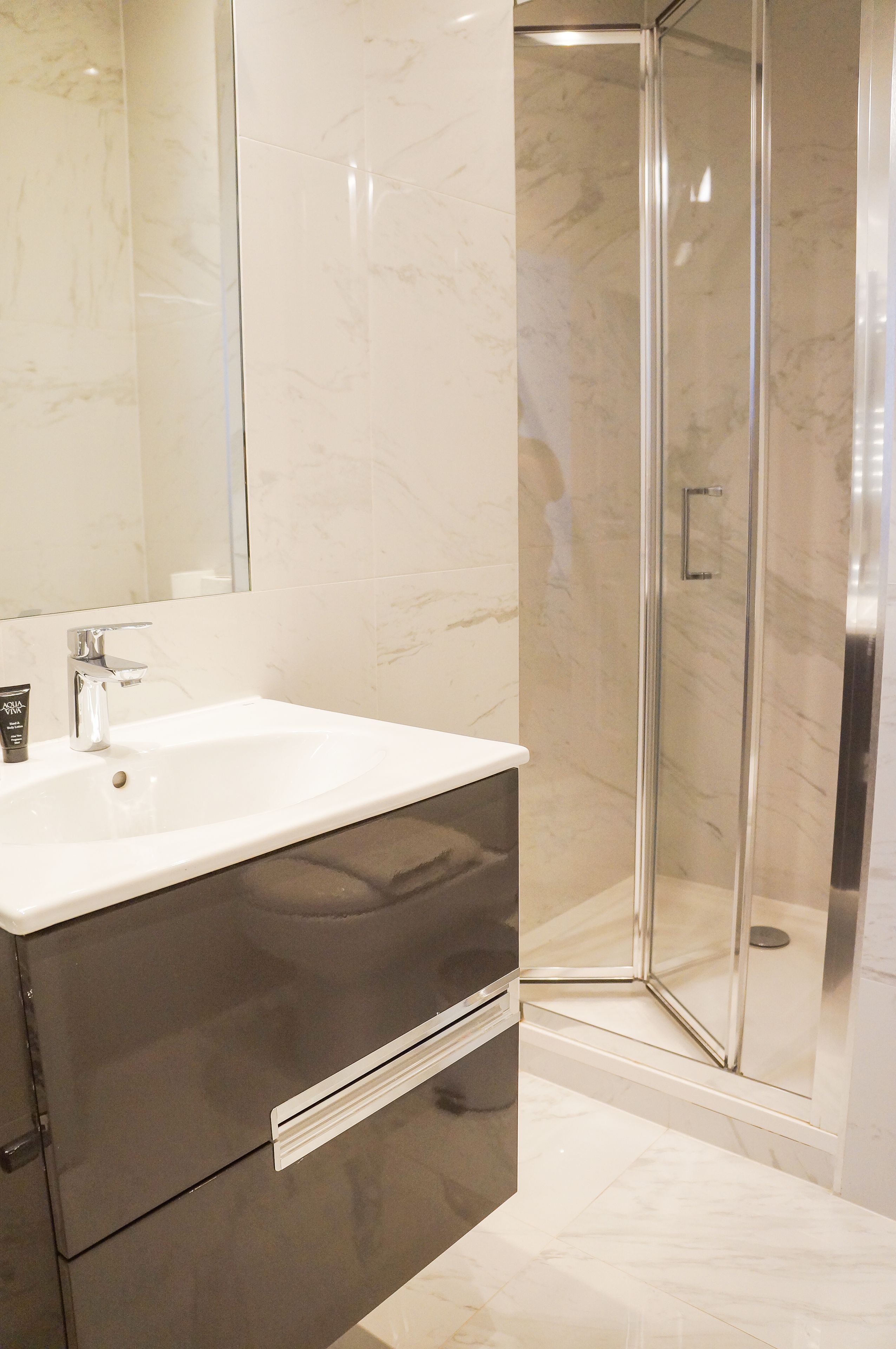 A bathroom with a white sink, dark cabinets, and a glass shower enclosure.