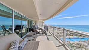 A balcony with a view of the beach, furnished with a sofa, chairs, and a table.