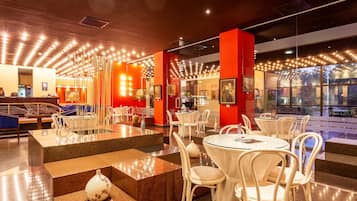 A modern restaurant with round tables and white chairs, a bar area, and a view through large windows.