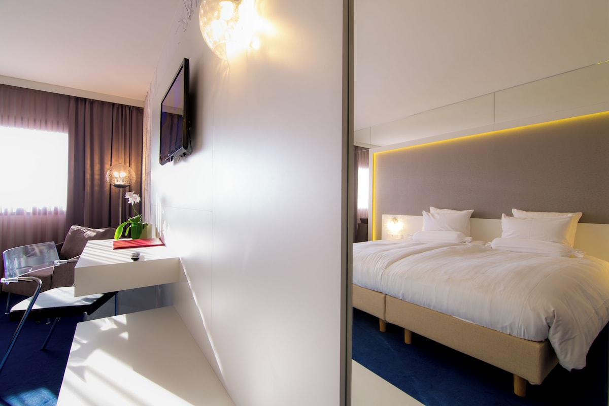 Una habitación de hotel moderna con cama, escritorio, silla y televisor montado en la pared.