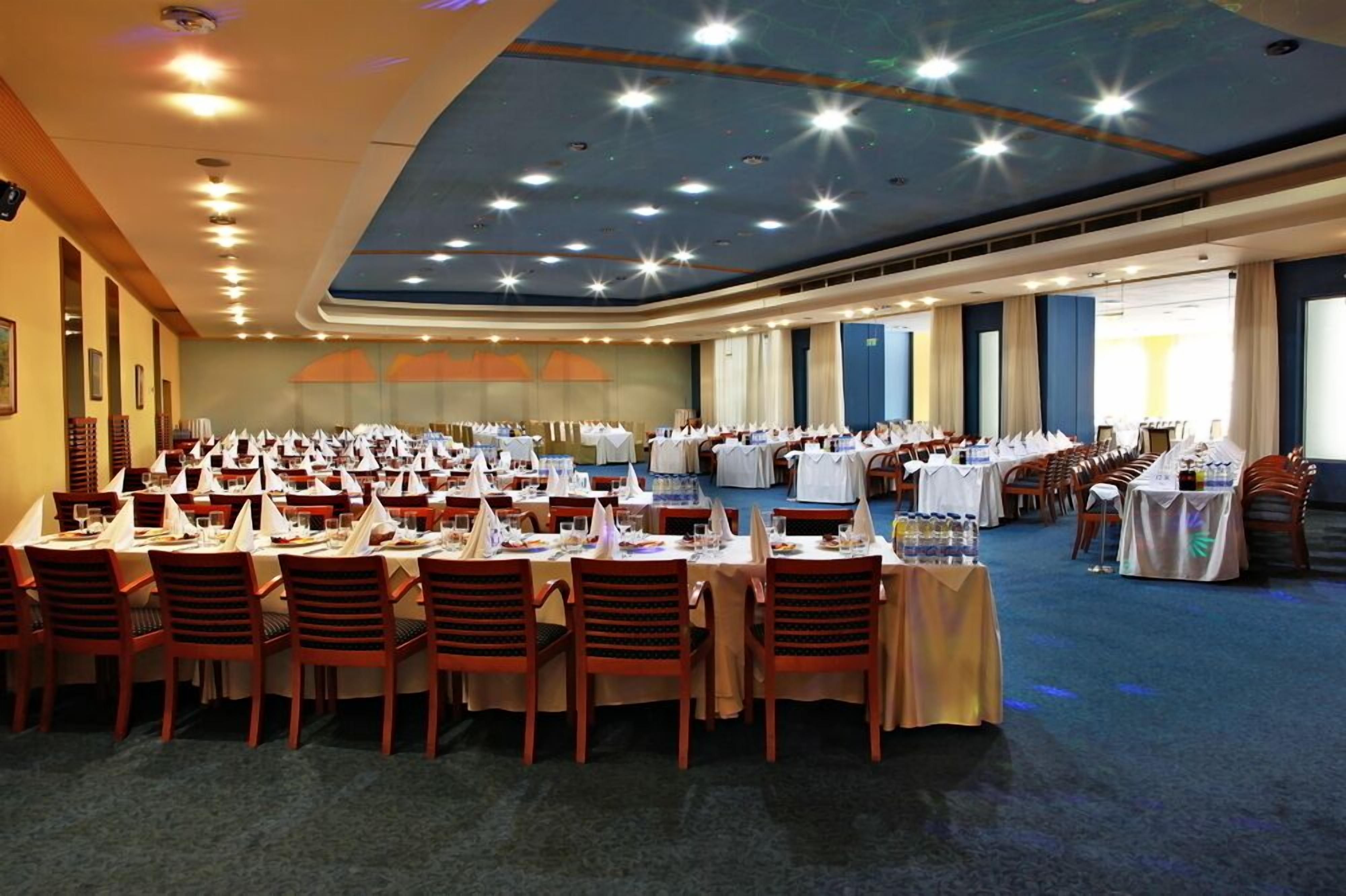 Un amplio salón de banquetes con varias mesas redondas, cada una con mantel blanco y sillas rojas.