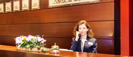 A reception desk with a sign that reads "RECEPTION" and a bell. There are framed certificates or awards on the wall behind the desk.