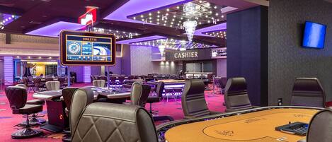 A casino floor with multiple gaming tables, a roulette wheel, and a cashier area.