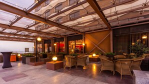 Una terraza en la azotea con mobiliario de mimbre, una zona de bar y una estructura de techo de cristal.