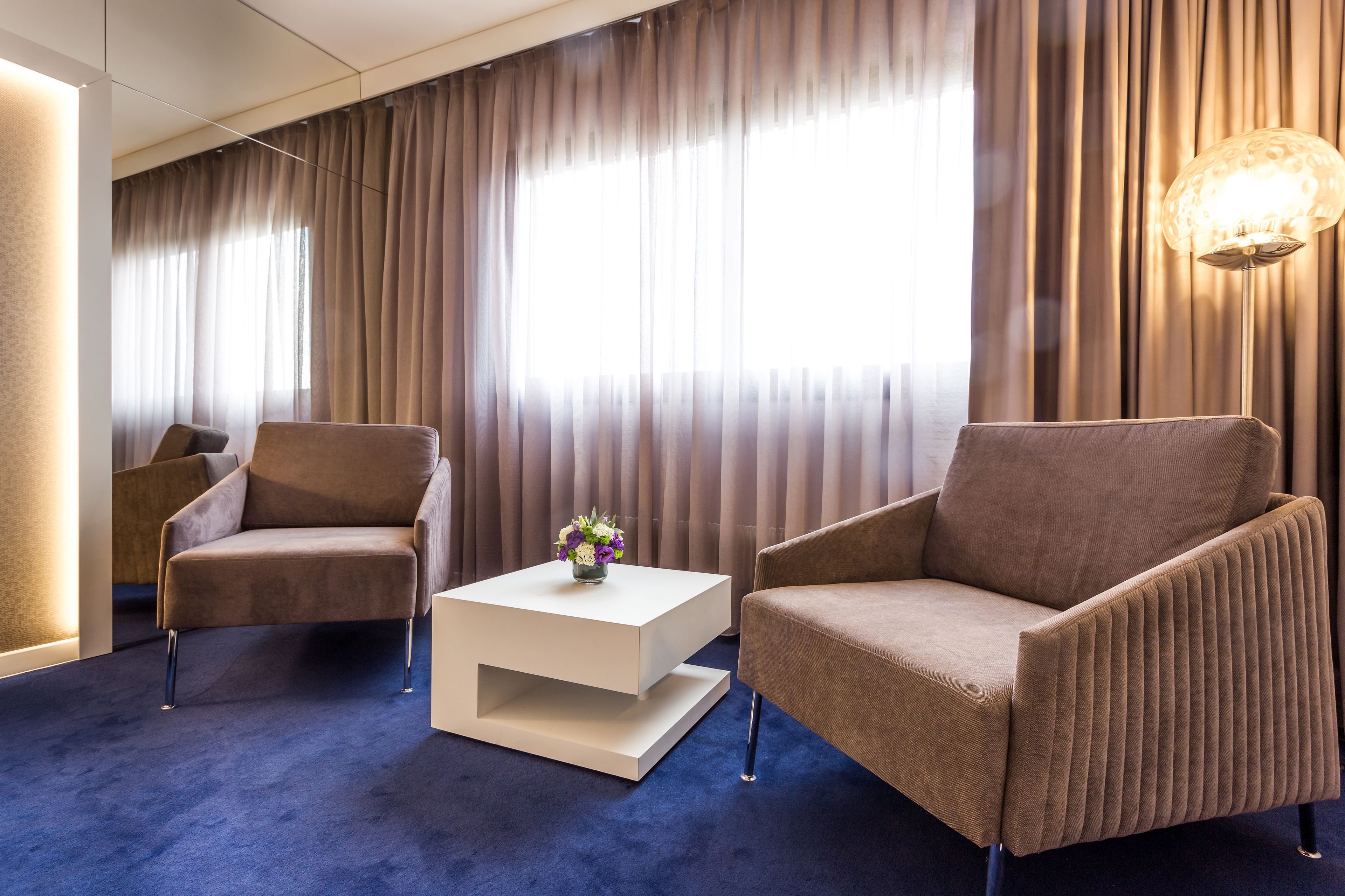 A modern hotel room with two armchairs, a white coffee table, and a decorative vase.