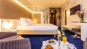 Una habitación de hotel con una cama, un escritorio, una silla, una mesa con desayuno y un televisor en la pared.