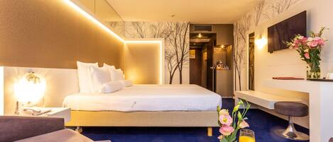 Una habitación de hotel con una cama, un escritorio, una silla, una mesa con desayuno y un televisor en la pared.