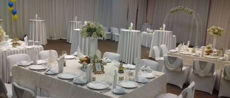 Un salón de banquetes con mesas redondas, manteles blancos y sillas cubiertas con tela blanca.