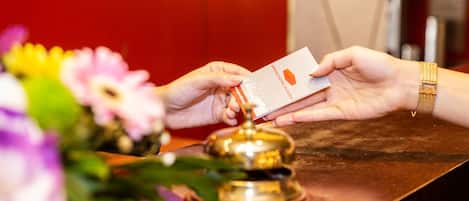 A hand holding a card at a reception desk with a bell and a flower arrangement.