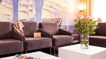 A modern lounge area with three dark brown sofas, a white coffee table with magazines, and a vase of pink roses.
