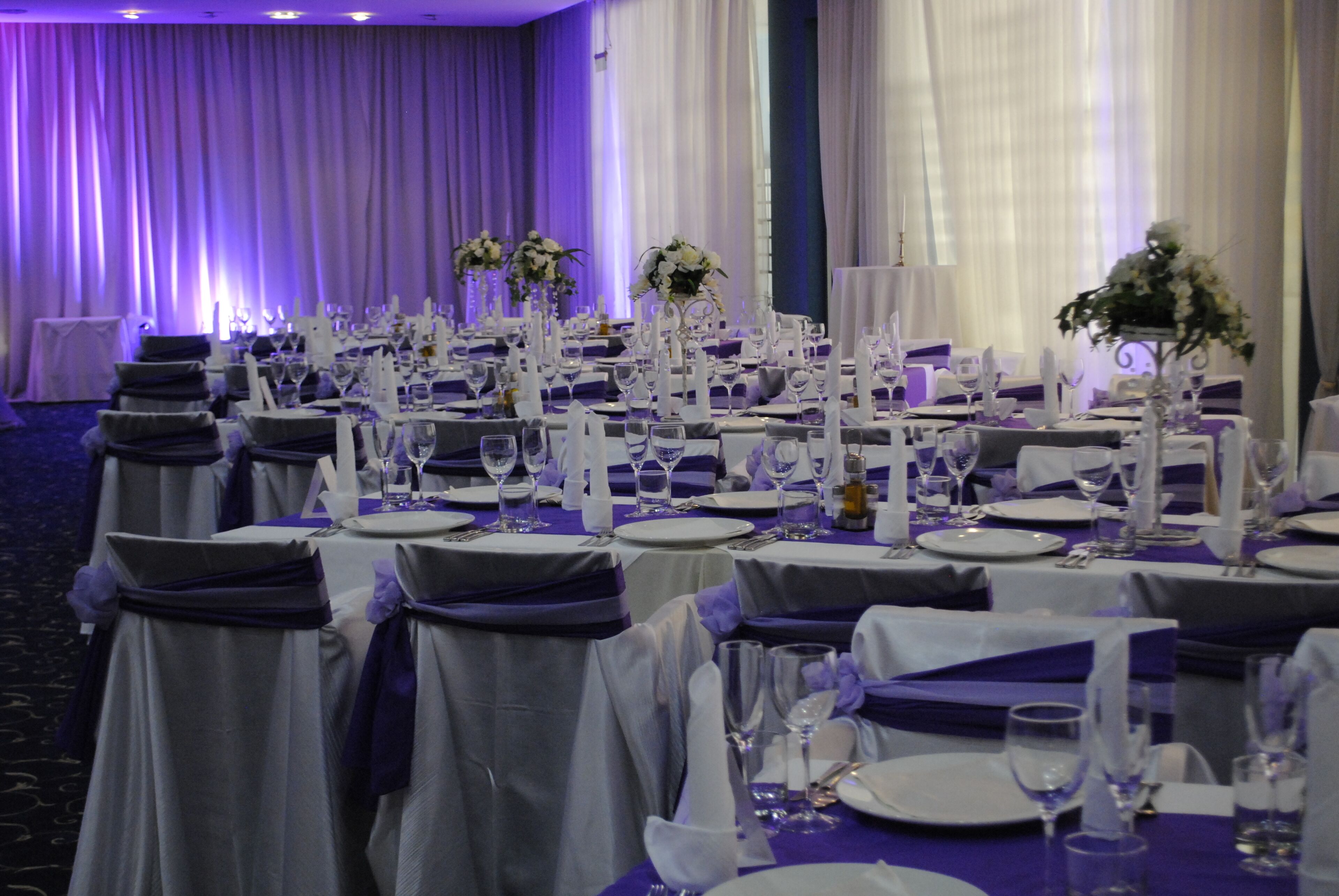 Un salón de banquetes con mesas dispuestas para un evento formal, destacando manteles blancos, cubiertos de plata y centros de mesa florales.