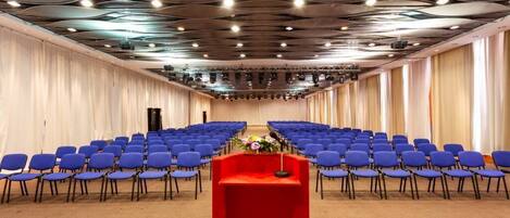 A conference room with rows of blue chairs, a red podium, and a modern ceiling design.
