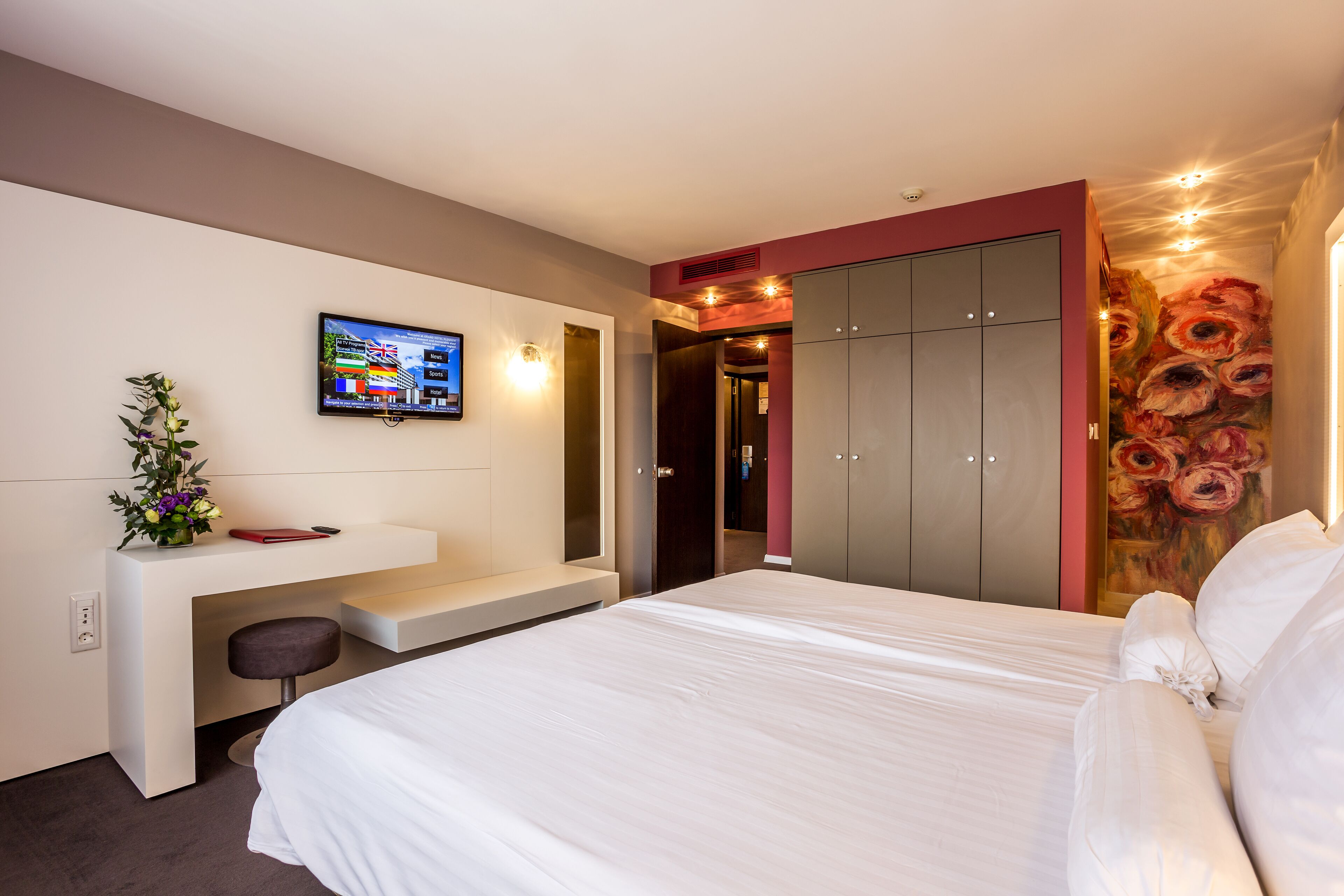 Una habitación de hotel moderna con una cama grande, un escritorio con silla, un televisor y un armario.