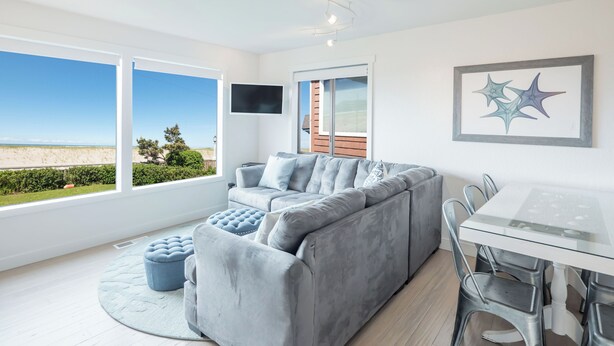 En moderne stue med en grå sofa, et glasbord og havudsigt.