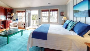 A bedroom with a large bed, a glass coffee table, a desk with a chair, and a view of the outdoors through a sliding door. - OCEAN VIEW: SAND HILL MANOR:  Seaside Vacation Homes, Inc. Managed (Gearhart)