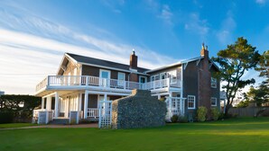 A two-story house with a stone fireplace, a balcony, and a well-maintained lawn. - OCEAN VIEW: SAND HILL MANOR:  Seaside Vacation Homes, Inc. Managed (Gearhart)